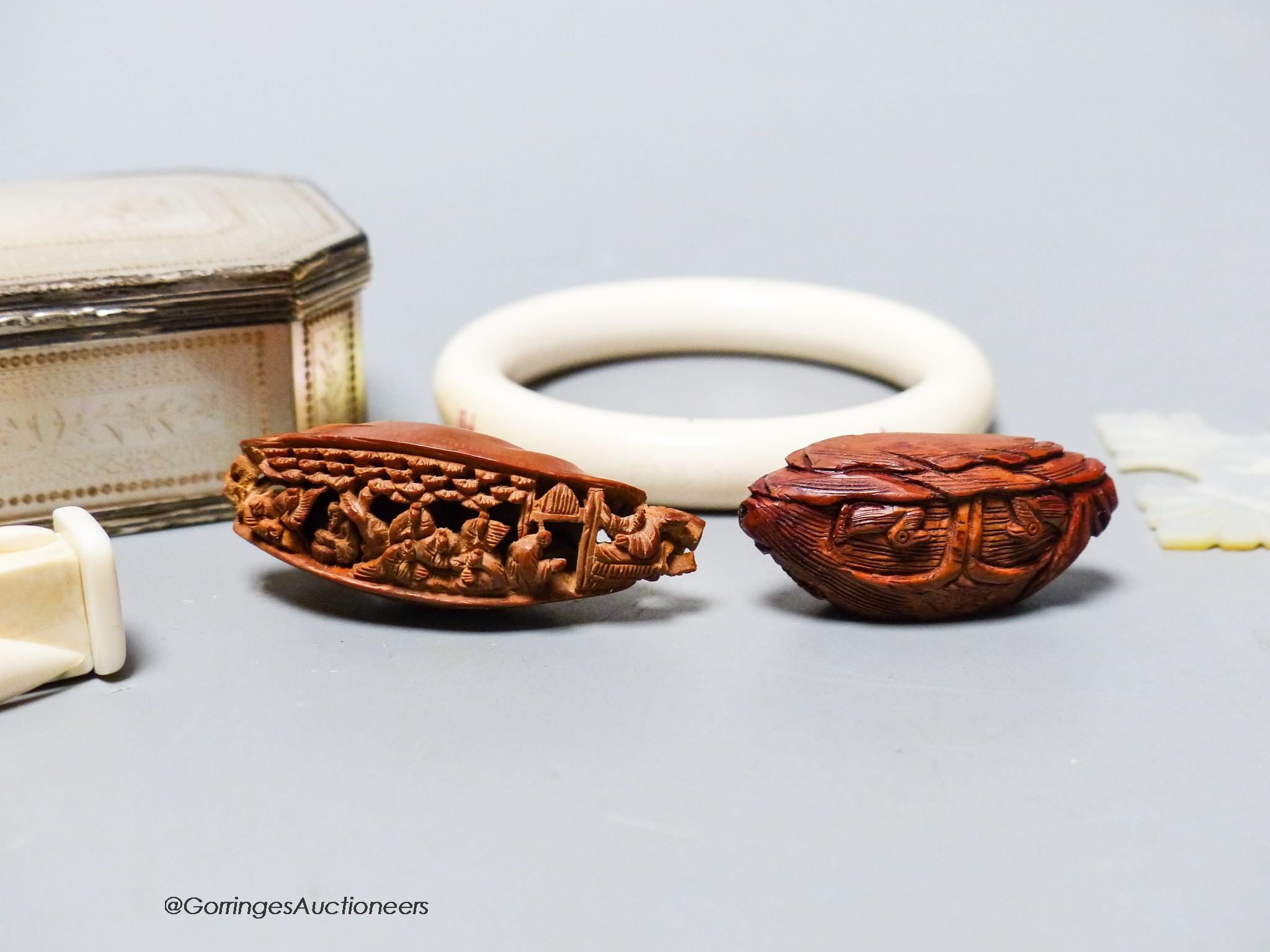 A 19th century panelled mother of pearl box together with a Chinese carved peach stone, a Chinese ivory bangle and a small worked bone multi-tool